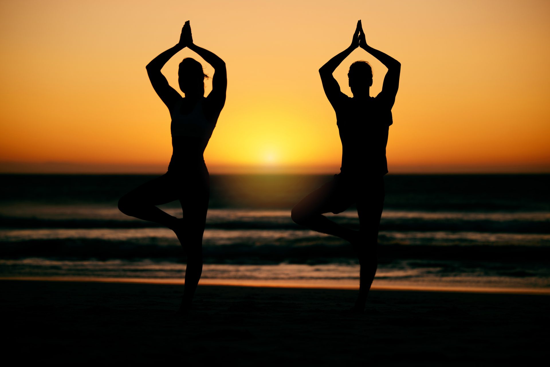 2 Frauen machen Joga am Strand im Sonnenuntergang zur Vorbereitung und Nachsorge bei ästhetischen Behandlungen